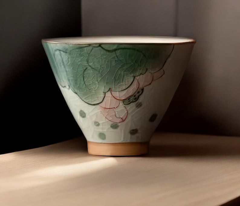 May include: A white ceramic bowl with a green and pink floral design. The bowl has a wide rim and a rounded bottom.
