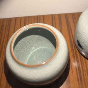 May include: A light blue ceramic jar with a light brown rim. The jar has a crackled glaze finish.