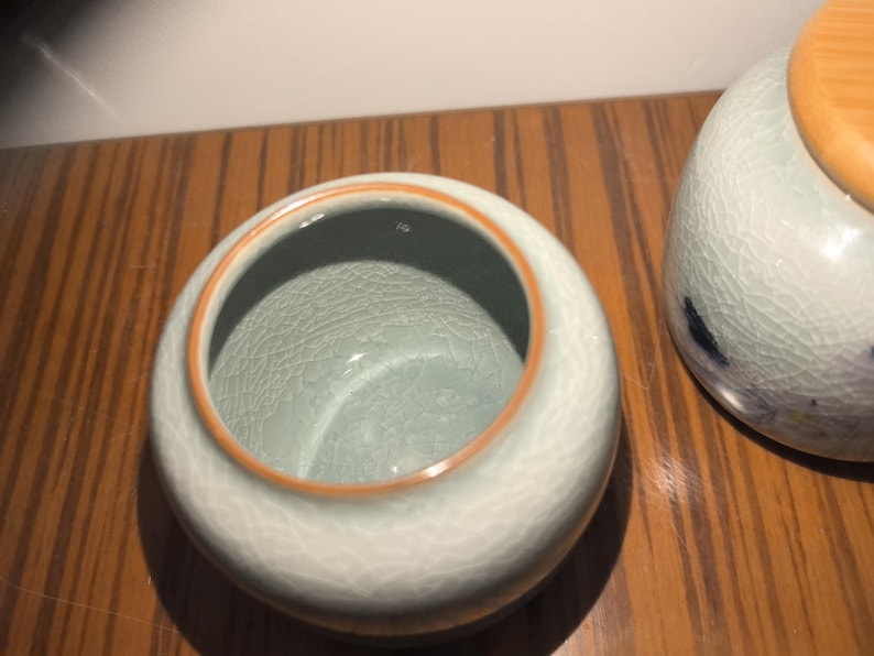 May include: A light blue ceramic jar with a light brown rim. The jar has a crackled glaze finish.