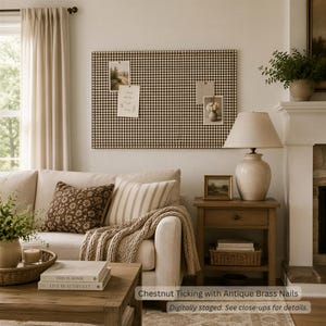 May include: A rectangular wall-mounted bulletin board covered in brown and white gingham fabric, featuring antique brass nailhead trim along the edges. The board displays three pinned photographs and notes on its surface.