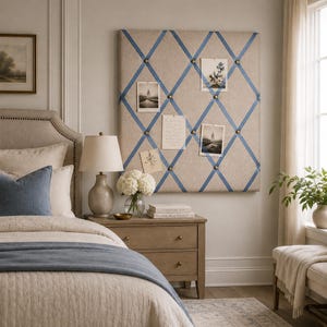 May include: A square beige fabric memo board featuring a blue ribbon lattice pattern secured with brass-toned upholstery tacks. The board displays four photographs and a handwritten note tucked into the diamond-shaped ribbon sections.