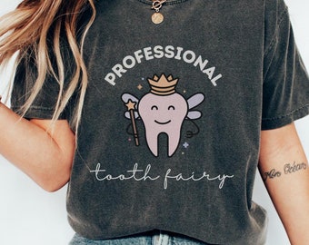 Może przedstawiać: Szary t-shirt z nadrukiem wróżki zębuszki. Wróżka zębuszka ma na sobie koronę i skrzydła. Na koszulce widnieje napis "Profesjonalna wróżka zębuszka".