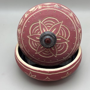 Peut inclure: Un bol rond en céramique avec couvercle de couleur rose poussiéreux. Le couvercle présente un motif floral sculpté et un bouton foncé. Le bord et le couvercle du bol sont décorés d'un motif sculpté. L'intérieur du bol est noir.