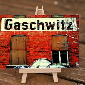 May include: A red brick building with two windows, one with a wooden door and the other with a glass window. The building has a white sign that says "Gaschwitz" in black letters.