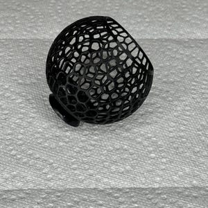 May include: A black, 3D-printed, spherical object with a honeycomb-like pattern. The object has a small, flat base and a rounded top. The intricate design creates a visually interesting texture. The object is likely a decorative item or a component of a larger design.