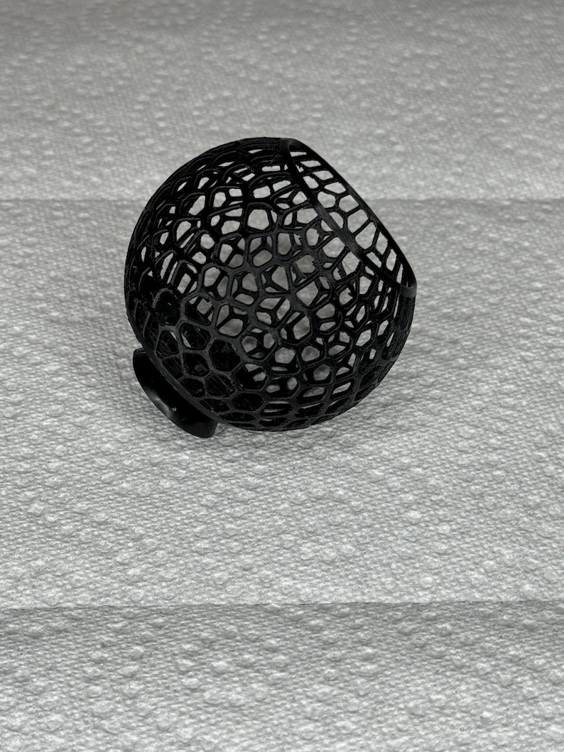 May include: A black, 3D-printed, spherical object with a honeycomb-like pattern. The object has a small, flat base and a rounded top. The intricate design creates a visually interesting texture. The object is likely a decorative item or a component of a larger design.