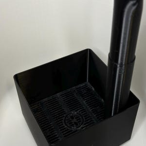 May include: A black plastic square container with a black plastic filter inside. A black plastic tube with a curved top is inserted into the container.