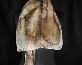May include: A brown and green silk scarf with a watercolor-like design. The scarf is folded and displayed on a black mannequin. The scarf is signed "Marlies 1997 Silk Craft".