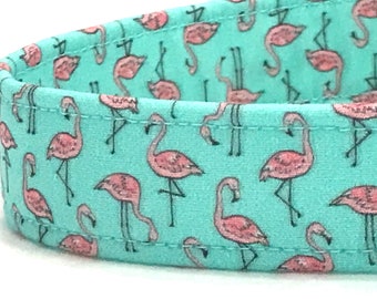 May include: A turquoise blue fabric with a repeating pattern of pink flamingos. The flamingos are standing on one leg with their necks bent in an S shape.