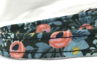 Könnte beinhalten: Nahaufnahme eines dunkelgrünen Stoffhundehalsbandes mit einem Blumenmuster mit rosa und blauen Blüten. Das Halsband hat eine schwarze Naht.