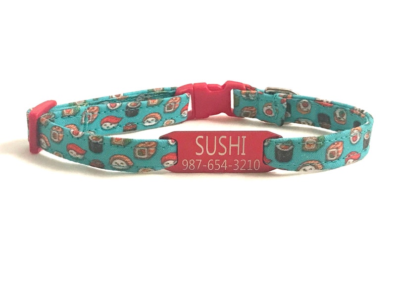 May include: A red cat collar with a turquoise fabric pattern of sushi rolls. The collar has a red engraved tag that reads "SUSHI 987-654-3210".
