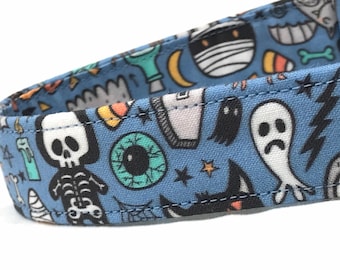May include: A blue cotton dog collar with a Halloween-themed print featuring ghosts, skulls, eyeballs, and candy corn.