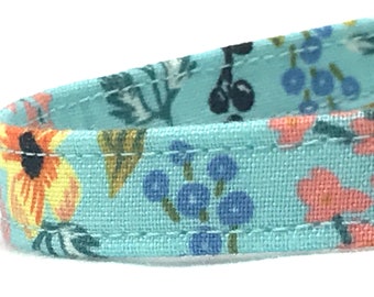 Könnte beinhalten: Nahaufnahme eines hellblauen Stoffes mit Blumenmuster. Der Stoff hat eine weiße Nahtdetail entlang der Kante. Das Muster enthält kleine blaue Blumen, orangefarbene Blumen und grüne Blätter.