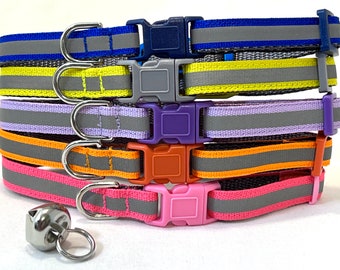 May include: Five colorful dog collars with reflective strips and silver D-rings. The collars are stacked on top of each other, with the top collar being blue, followed by yellow, purple, orange, and pink. A silver bell is attached to the bottom collar.