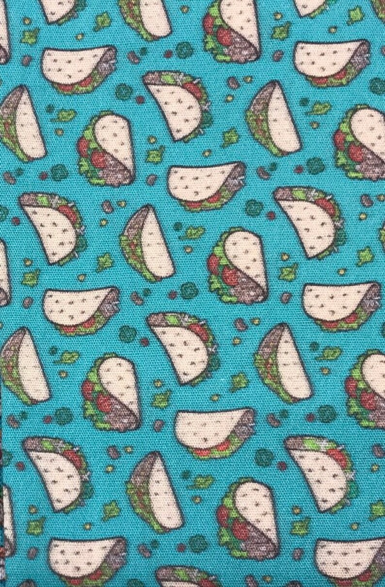 May include: A blue fabric with a repeating pattern of white tacos with green lettuce and brown meat fillings.