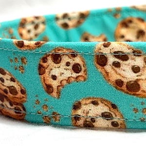 May include: A turquoise blue fabric collar with a repeating pattern of chocolate chip cookies.