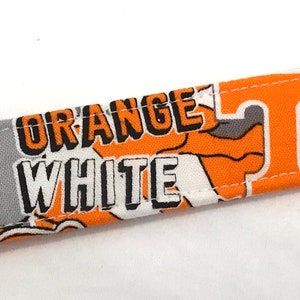 Puede incluir: Tela naranja y blanca con las palabras "ORANGE WHITE" y una "T" estilizada impresa en ella.