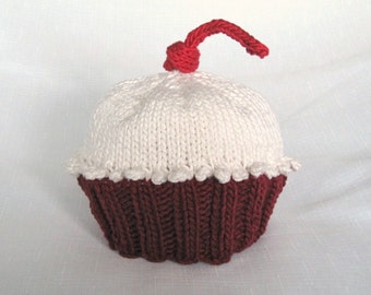 May include: White knitted cupcake hat with a red cherry on top. The hat has a red and white striped pattern.
