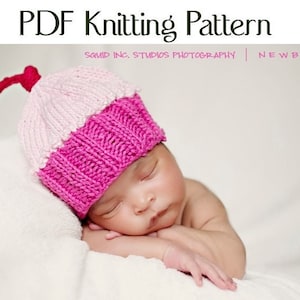 May include: A pink and white knitted cupcake hat with a red cherry on top. The hat is worn by a sleeping baby.