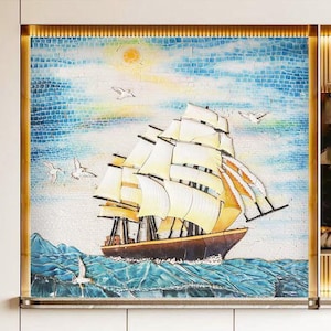 Op de afbeelding: Een mozaïekkunstwerk dat een wit zeilschip met bruine masten en zeilen toont, tegen een blauwe en witte mozaïekachtergrond. Het schip vaart op een blauwe en groene mozaïekzee met witte vogels die erboven vliegen.
