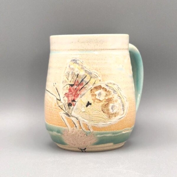 Butterfly alights on a flower on this handmade and hand-painted ceramic mug
