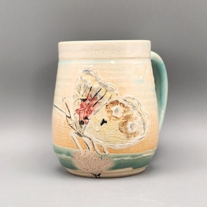 Butterfly alights on a flower on this handmade and hand-painted ceramic mug