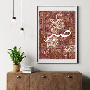 May include: A white framed print with a collage of red, brown, and cream patterned rugs. The word "حب" is written in white Arabic calligraphy over the collage.
