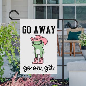 Puede incluir: Una bandera de jardín blanca con una rana verde que lleva un sombrero de vaquero rosa y el texto "GO AWAY... go on, git".