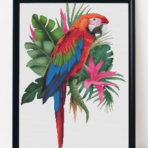 May include: A framed cross-stitch of a vibrant macaw perched on a branch, surrounded by lush green leaves and pink flowers. The parrot features red, blue, and green plumage, set against a white background.