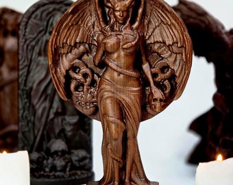 May include: A wooden sculpture of a winged female figure with horns, holding a skull in one hand and a snake in the other. The sculpture is carved in a dark wood and has a detailed design. The sculpture is standing on a wooden base with the inscription "73737".