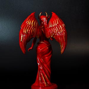 May include: Red figurine of a winged demon with gold accents. The demon is standing with its wings spread out behind it.