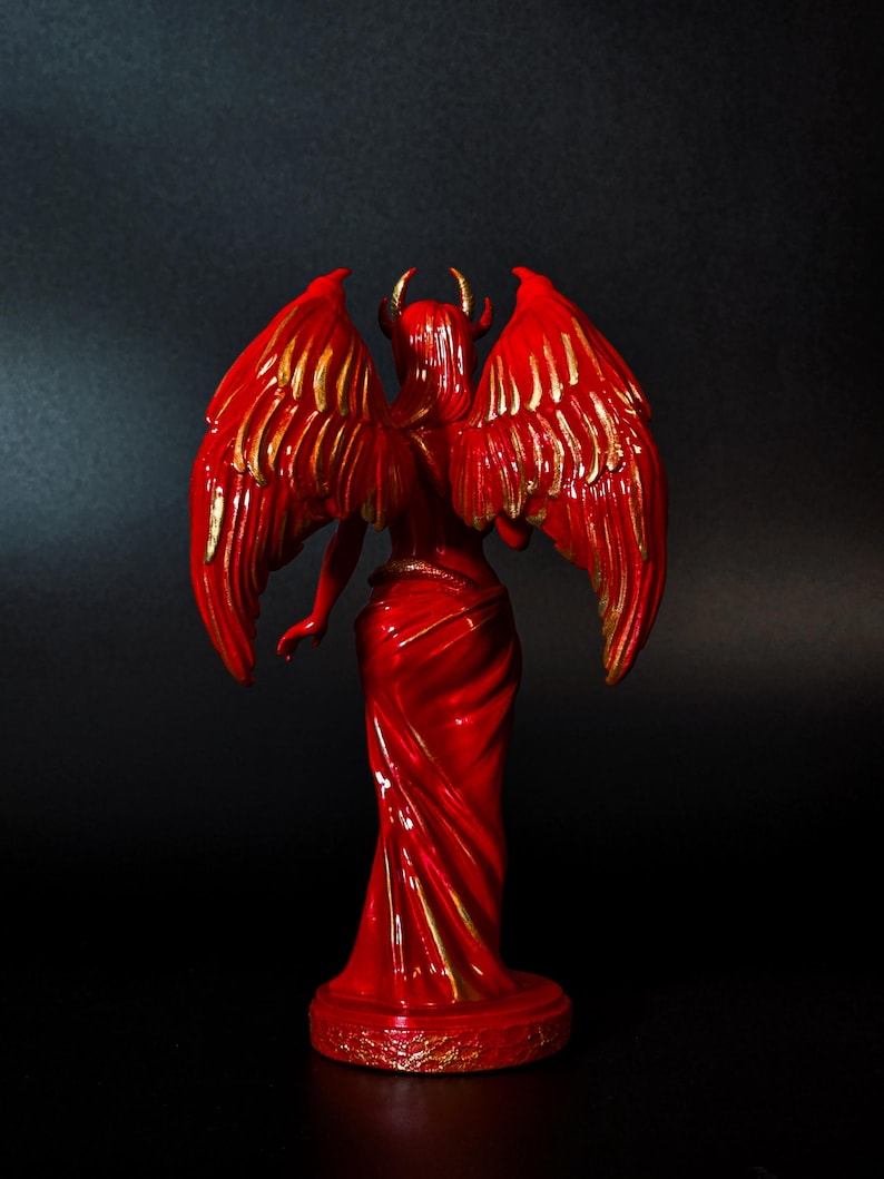 May include: Red figurine of a winged demon with gold accents. The demon is standing with its wings spread out behind it.