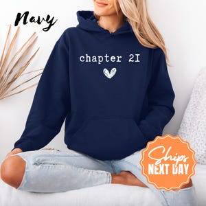 May include: Navy blue hooded sweatshirt with the text "chapter 21" and a white heart graphic. The word "Navy" is written in cursive on the upper left. The sweatshirt has a front pocket and a drawstring hood.