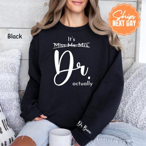 May include: Black sweatshirt with white text that reads "It's Dr. actually." The sleeve has the text "Dr. Brew." The sweatshirt is a crew neck style.