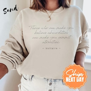 May include: Sand-colored sweatshirt with the quote "Those who can make you believe absurdities can make you commit atrocities." by Voltaire. The word "Sand" is written in a cursive font in the upper left corner.