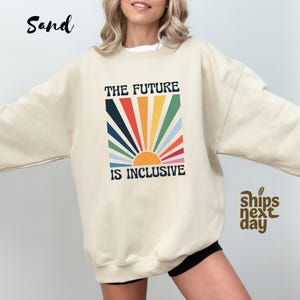 May include: A beige sweatshirt with a rainbow sun graphic and the text "The Future is Inclusive".