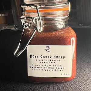 May include: A small glass jar filled with reddish-brown honey. The jar has a metal clasp and an orange rubber seal. A white label reads "Rose Cacao Honey" with ingredient details and a 2.5 oz measurement.