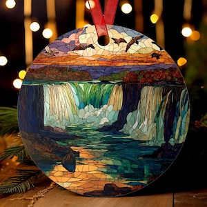 May include: Round ornament featuring a stained-glass style depiction of a waterfall scene with birds in flight. The artwork showcases a vibrant sunset with shades of orange, blue, and green. A red ribbon is attached for hanging.