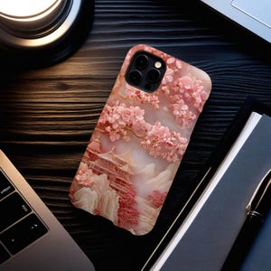 May include: A phone case featuring a 3D relief design of a Japanese pagoda scene with cherry blossoms in shades of pink and white. The case has a marble-like texture and a camera cutout.