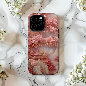 May include: A phone case featuring a pink and gold illustration of a Japanese landscape. The design includes cherry blossoms, pagodas, and mountains. The case has a glossy finish and a camera cutout.