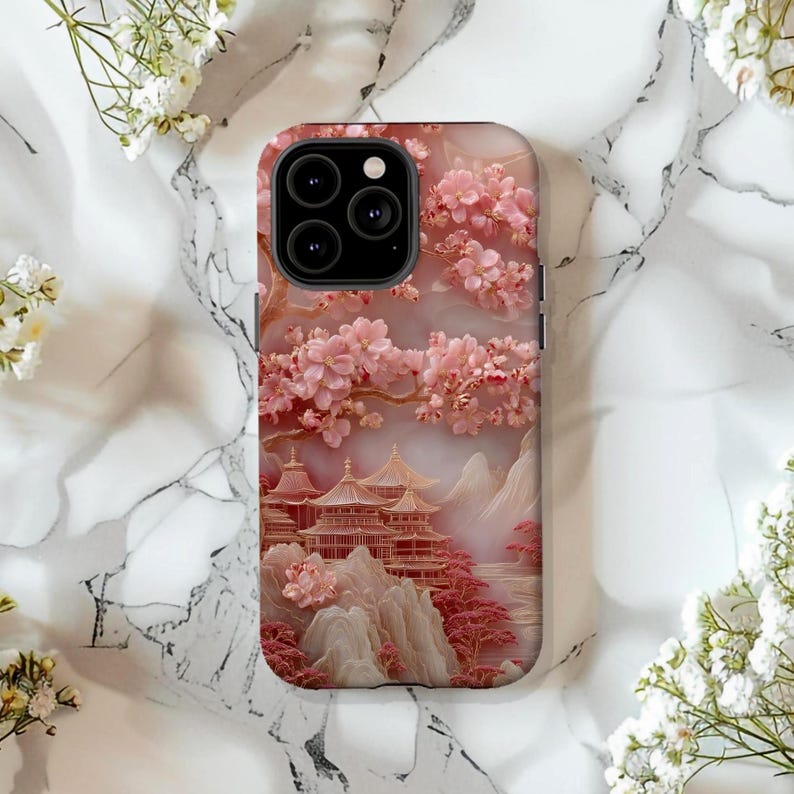 May include: A phone case featuring a pink and gold illustration of a Japanese landscape. The design includes cherry blossoms, pagodas, and mountains. The case has a glossy finish and a camera cutout.