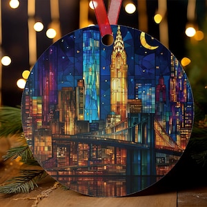May include: Circular Christmas ornament with a stained-glass effect showing the New York City skyline at night. The design includes the Brooklyn Bridge, skyscrapers, and a crescent moon, with a red ribbon for hanging.
