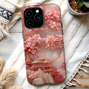 May include: A phone case featuring a pink and gold relief design of a Japanese pagoda, mountains, and cherry blossoms. The case has a glossy finish and a raised floral texture, with a soft pink and white background.