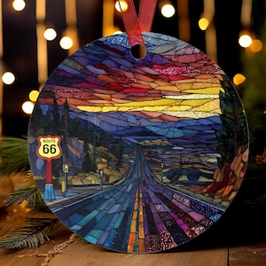 Puede incluir: Adorno redondo con un diseño de vidriera de la Ruta 66 al atardecer. La imagen incluye una carretera, montañas y un letrero que dice "Route 66". El adorno tiene una cinta roja para colgar.