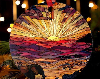 May include: Round Christmas ornament featuring a stained-glass design of an African savanna sunset. The ornament depicts a vibrant sunset with elephants, zebras, and other wildlife. A red ribbon is attached for hanging.