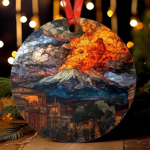 May include: Round Christmas ornament featuring a stained-glass style depiction of a volcanic eruption over a city. The ornament has a red ribbon for hanging. The artwork includes shades of orange, blue, gray, and brown.