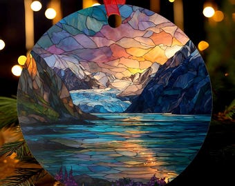 May include: Round Christmas ornament featuring a stained-glass style depiction of a mountain landscape with a glacier and lake. The artwork showcases a sunset with vibrant colors of orange, purple, and blue. A red ribbon is attached for hanging.