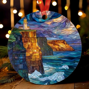 May include: Round Christmas ornament featuring a lighthouse on a cliffside, rendered in a stained-glass style. The design includes a blue ocean with white waves, a colorful sky, and a red ribbon for hanging. The ornament has a glossy finish.