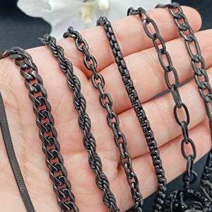 Op de afbeelding: Een set van zes zwarte kettingen met verschillende schakelstijlen, waaronder een curb-ketting, een touwketting, een box-ketting, een kabelketting en een figaro-ketting.