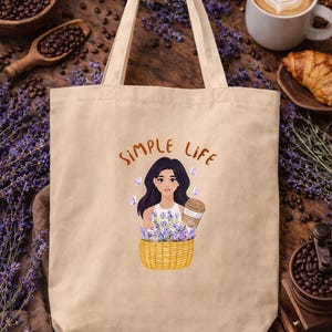 Bolsa de tela color beige con ilustración de chica tras una cesta con lavanda y café con el texto "Simple Life" sobre fondo cálido de madera y taza de café.